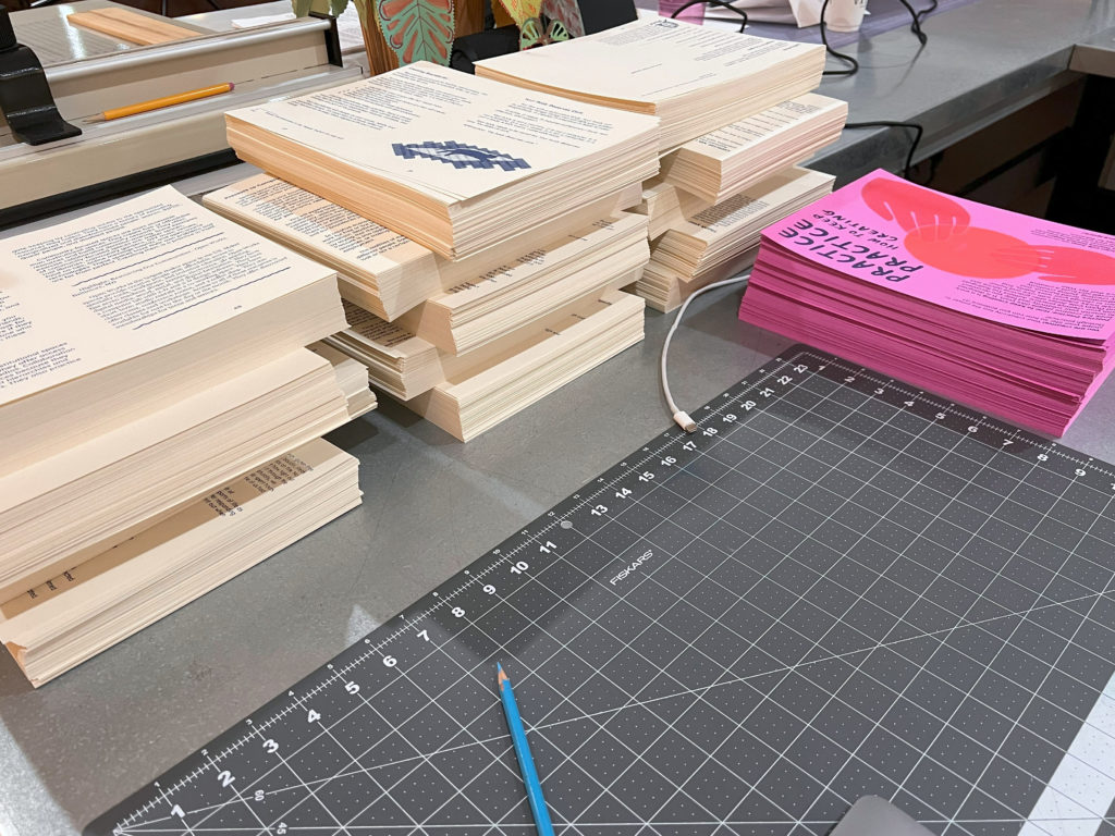 Printed pages are arranges in neat, tall stacks around the edge of a rubber cutting mat.